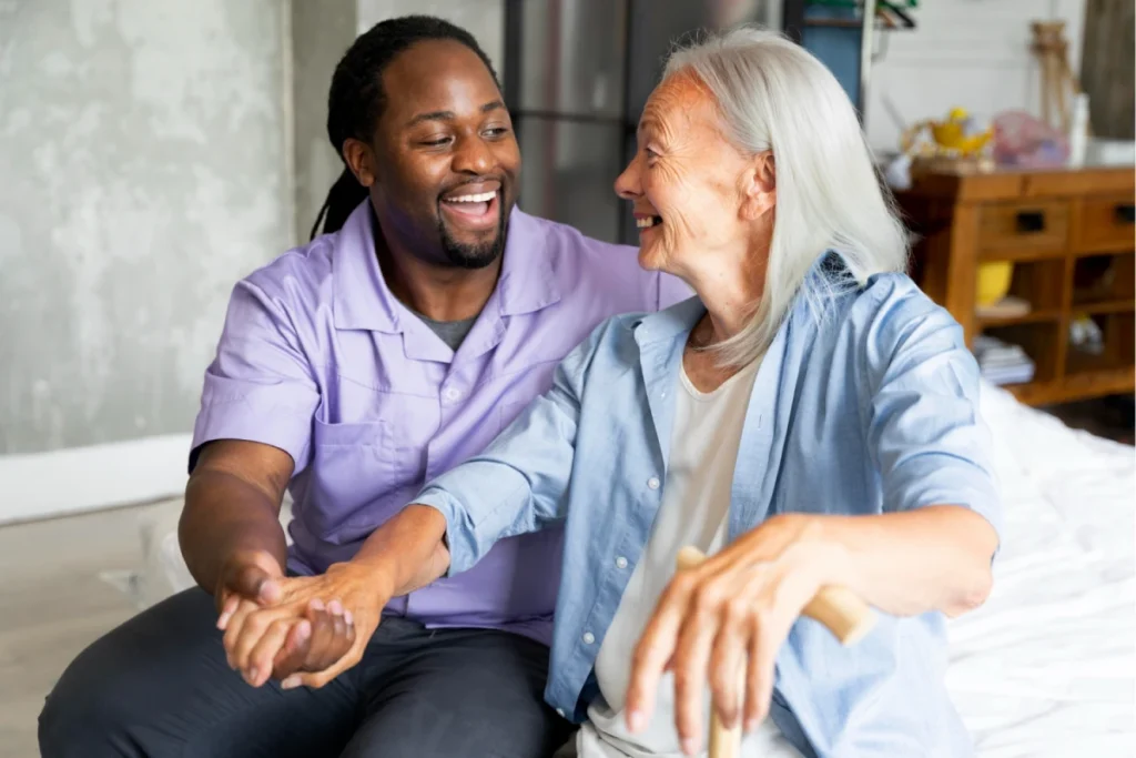 A smiling elderly woman sitting on a bed, engaging in a joyful conversation with a cheerful male