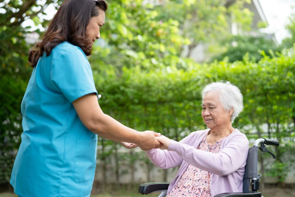 Caregiver holding hands with elderly woman outdoors.