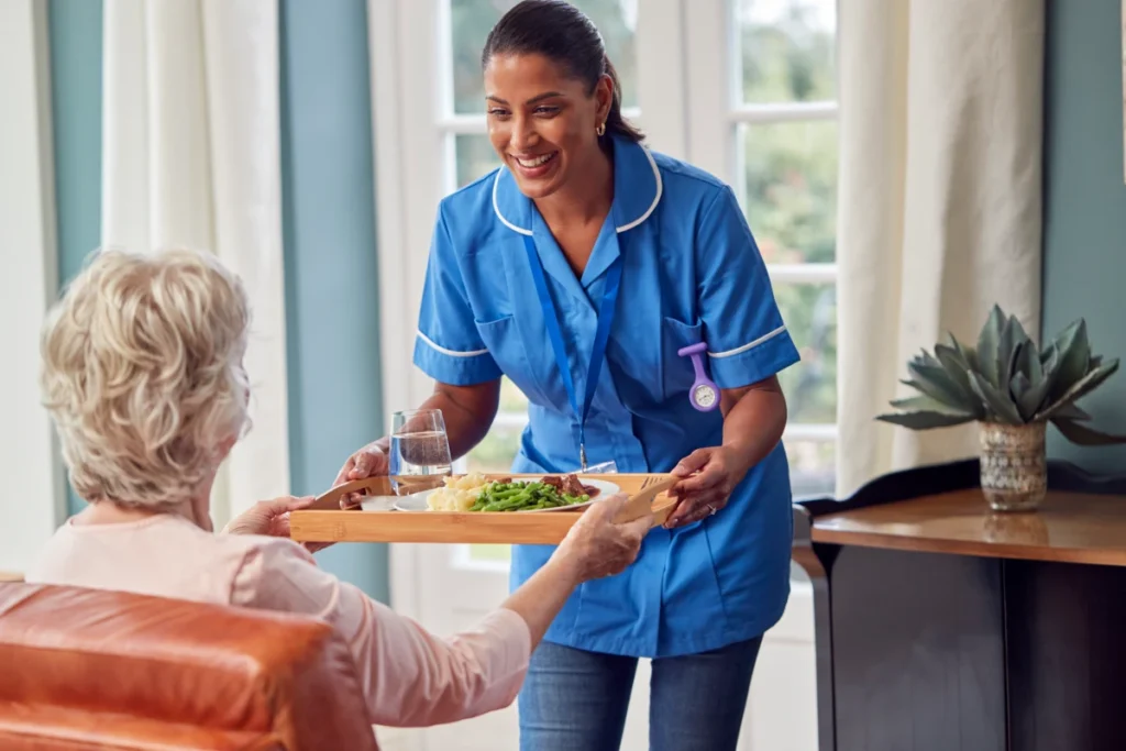Caregiver serving meal to elderly woman.