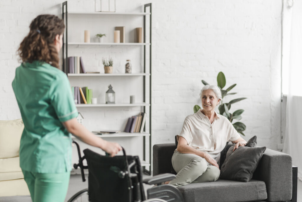 Caregiver approaching seated elderly woman smiling.