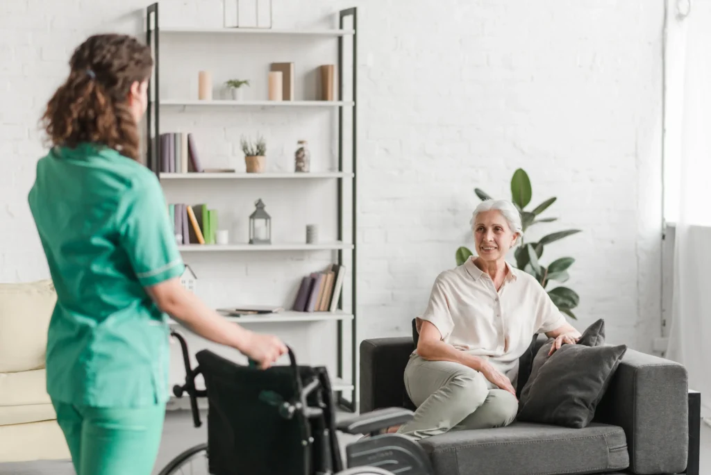 Caregiver approaching seated elderly woman smiling.