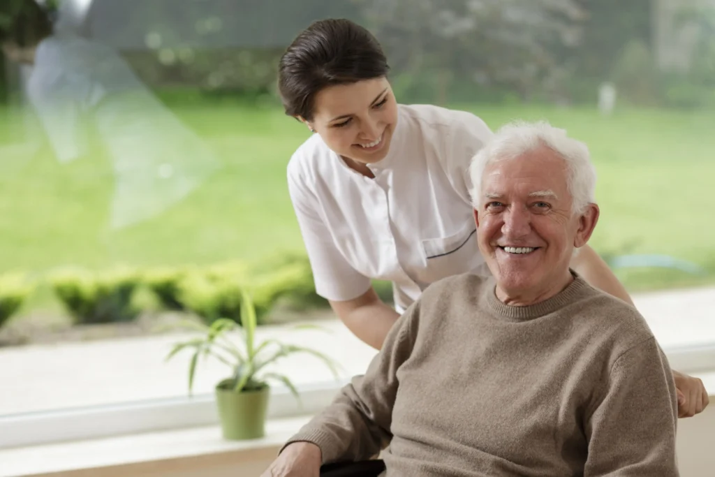 Caregiver supporting smiling elderly man indoors.