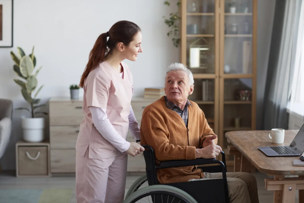 Caregiver assisting elderly man in wheelchair indoors.