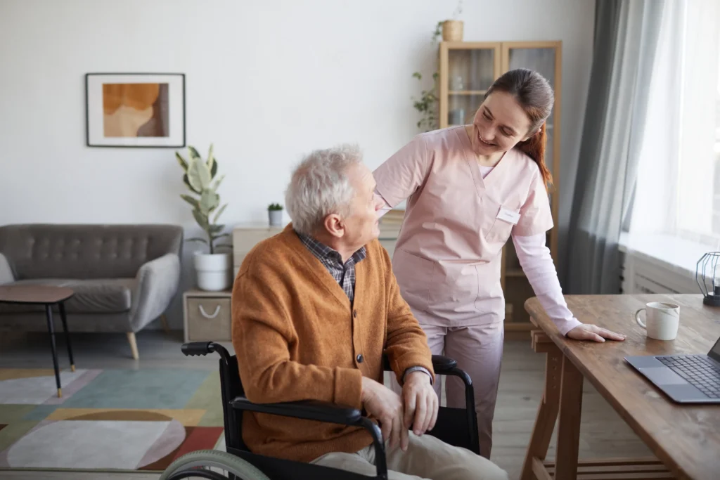 Caregiver talking with elderly man in wheelchair at home.