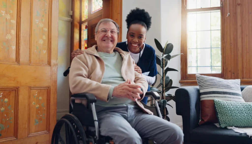 Caregiver smiling with elderly man in wheelchair at home.
