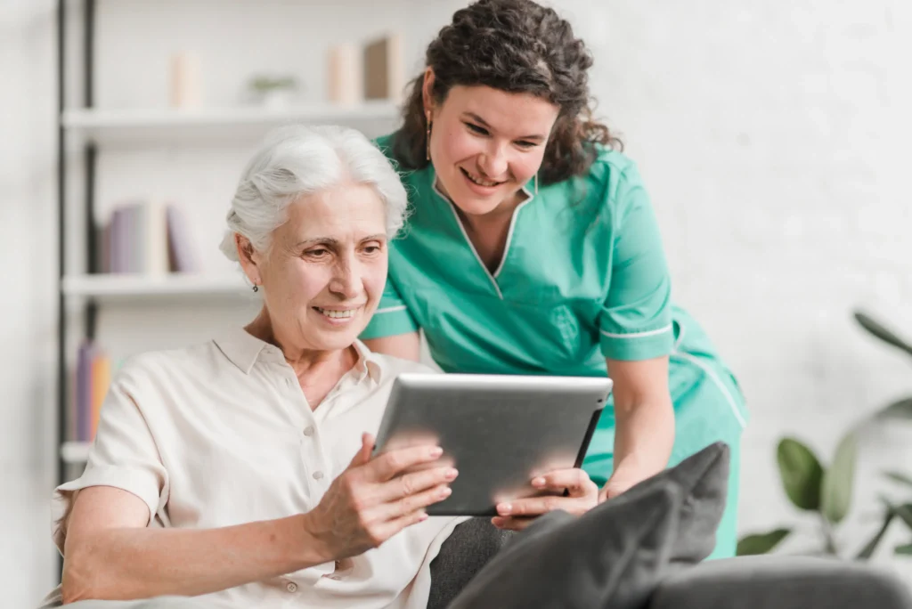 Caregiver helping elderly woman use tablet.