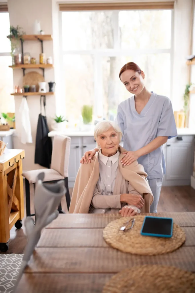Caregiver supporting elderly woman in kitchen.