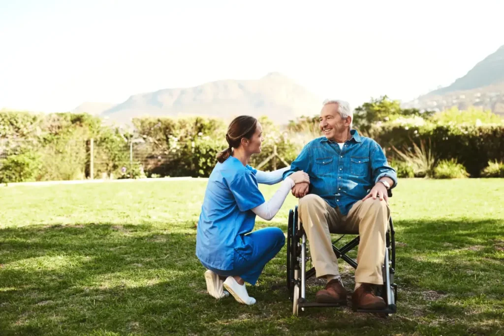 Caregiver assisting elderly man outdoors wheelchair.