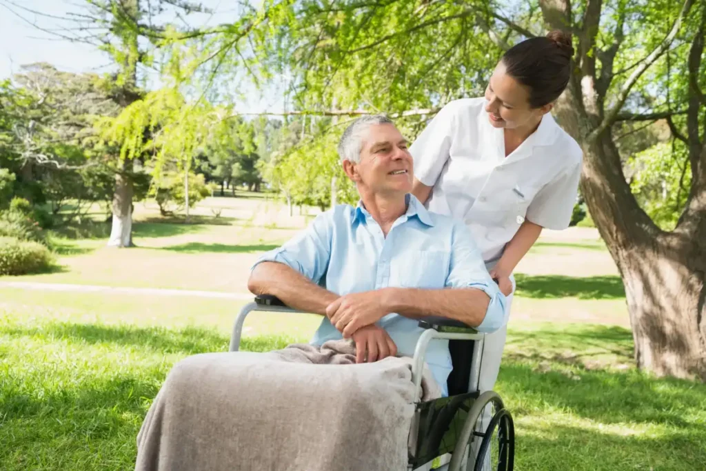 Caregiver pushing elderly man outdoors wheelchair.