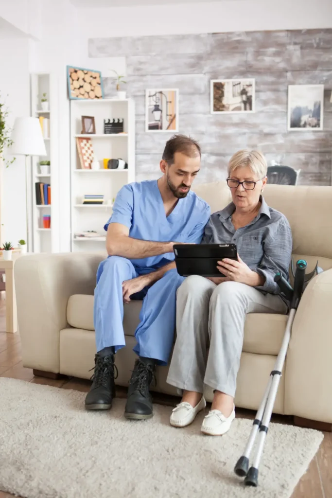 Caregiver assisting elderly woman with tablet on couch.